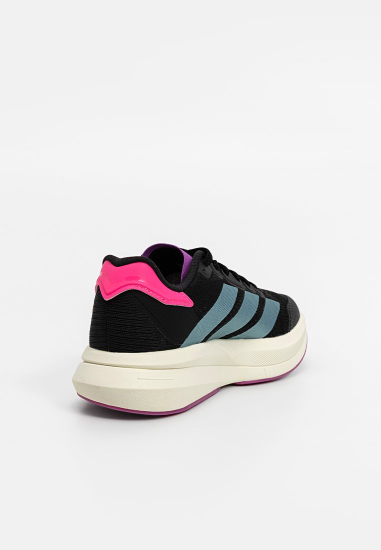 Zapatillas negras con tres franjas teal, un contrafuerte en rosa y púrpura, y una entresuela blanca con una suela rosa. Parte superior de tela texturizada.