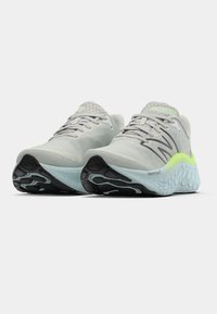 Par de sapatilhas de corrida cinza claro com solas pretas, entressolas azuis, detalhes em verde néon e cabedais em tecido de malha, vistos de frente.