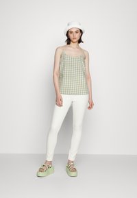 Top de alças fino em padronagem xadrez verde e branco, combinado com calças brancas justas e sandálias plataforma verdes. Um chapéu branco completa o visual.