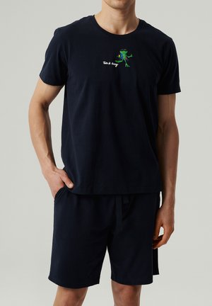 Granatowy t-shirt z bawełny z okrągłym dekoltem i krótkimi rękawami, z grafiką żaby i napisem "Nie przejmuj się." Dopasowany do granatowych szortów.