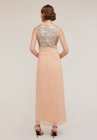 O rochie de seară lungă, de culoare piersică pală, cu un corset ajustat ce prezintă un design cu paiete argintii, talie strânsă și o fustă evazată.