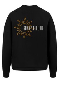 Black sweatshirt featuring a large yellow sun graphic and the text "KEEP YOUR SUNNY SIDE UP" on the back. Soft fabric, ribbed cuffs.