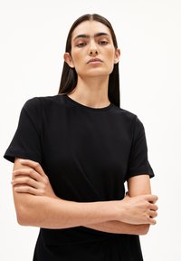 Schwarzes Kurzarm-T-Shirt mit rundem Ausschnitt, das eine glatte Textur und eine subtile Drehung in der Taille aufweist.