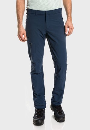 Marineblaue Outdoor-Hosen aus leichtem, flexiblem Stoff. Mit Reißverschlusstaschen und verstärkten Kniebereichen. Tragen mit schwarzen Wanderschuhen.