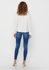 Vit, texturerad skjorta med långa ärmar som kombineras med blå skinny jeans och klara blockklackar. Skjortan har vertikala ränder och knäppta manschetter.
