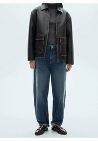 Veste en cuir noir avec des coutures marron, deux poches avant, pull gris en dessous, jeans bleu ample, chaussures marron.