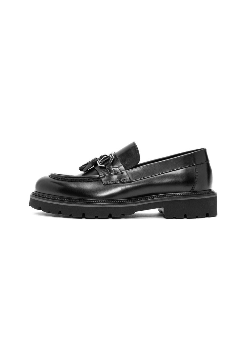 Mocasines de piel negra con una correa texturizada y detalles de hardware en plata. Presentan una suela de goma gruesa y un acabado liso y pulido.
