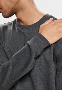 Donkergrijze sweatshirt met een ronde hals, lange mouwen en geribbelde manchetten. De stof lijkt zacht en is lichtjes textuur.