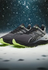 Scarpe da corsa nere con upper in mesh testurizzato, dotate di accenti riflettenti e una suola in gomma verde. Progettate per il comfort e le prestazioni.
