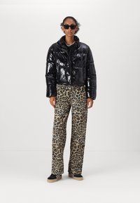 Černá prošívaná krátká bunda s lesklým povrchem, spárovaná s širokými kalhotami s leopardím potiskem. Modelka má na sobě černé boty a sluneční brýle.