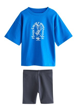 T-shirt bleu à manches courtes avec un motif skateboard blanc et du texte, associé à un short uni gris foncé jusqu'aux genoux.