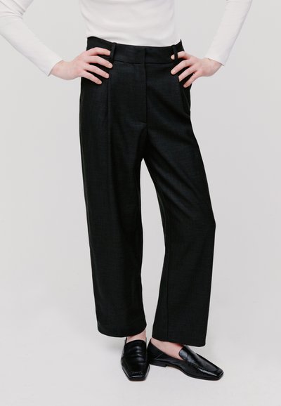 Pantaloni neri su misura con un design a gamba larga, tessuto texturizzato, vita alta e tasche laterali, abbinati a mocassini neri.