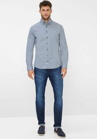 Camicia a bottoni blu e bianca con motivo, maniche lunghe, colletto, tasca frontale; abbinata a jeans in denim blu scuro e scarpe slip-on navy.