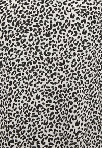 Vit tyg med ett svart leopardtrycksmönster, med oregelbundna former och varierande storlekar på fläckarna genom hela designen.