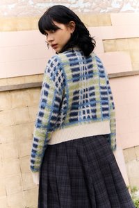Pulover scurt cu un model de carouri multicolore în nuanțe de albastru, verde și alb, având un tiv de culoare crem texturat și mâneci lungi, asortat cu o fustă cu carouri.