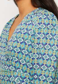 Monivärinen kuviollinen kangas, jossa on monimutkaisia kukkasuunnitelmia sinisen, oranssin ja vihreän sävyissä, v-pääntiellä ja pehmeällä tekstuurilla.