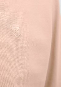 Svetloružová textúrovaná látka s jemnými diagonálnymi vzormi; obsahuje embosovaný geometrický logotyp v hornom ľavom rohu.