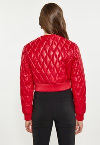Rode gewatteerde bomberjack met glanzende afwerking, ribgebreide manchetten en zoom, en korte lengte. Gestyled met strakke zwarte broek.