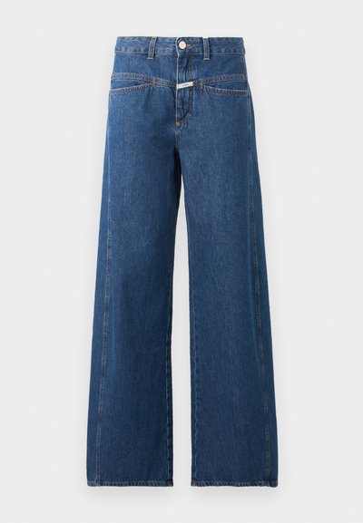 Jean bleu taille haute à jambes larges avec fermeture devant par bouton et fermeture éclair, poches avant et couture orange visible sur fond uni.