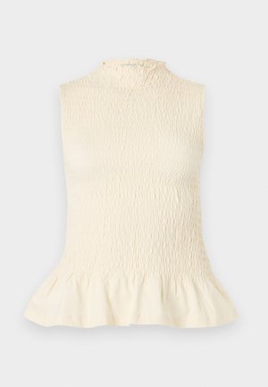 Blouse sans manches crème avec un col montant à volants, un tissu texturé smocké et un détail de bas évasé sur un fond uni.