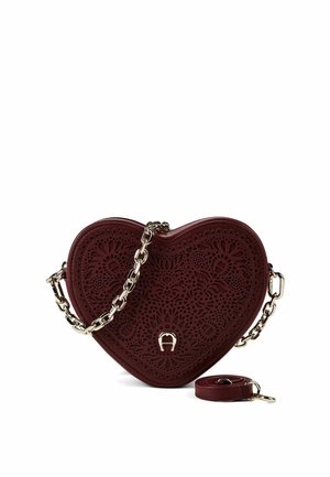 Sac à main rouge foncé en forme de cœur avec des motifs floraux découpés, bandoulière chaîne dorée attachée et bandoulière en cuir détachable assortie à côté.