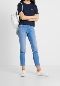 Navy crop T-shirt with small logo, light blue slim-fit jeans, and white sneakers, accompanied by a white backpack with accents.