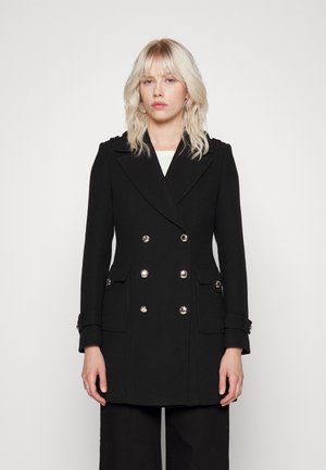 Manteau noir croisé avec de grands boutons en argent, poches latérales et détails aux épaules. Fabriqué en tissu texturé, coupe ajustée.