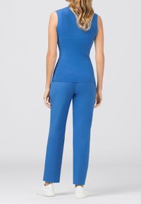 Blå ärmlös topp kombinerad med blå skräddarsydda byxor i slät tyg, med en figurnära silhuett och ren design. Vita sneakers kompletterar looken.