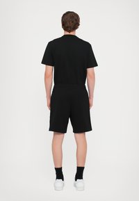 Black short-sleeve t-shirt and matching shorts, made of cotton, with an elastic waistband, viewed from the back, paired with white sneakers.