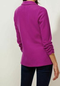 Upnutý fialový dlouhý rukáv s límečkem, na rukávech se shromážděnými detaily a hladkou texturou. Jednoduchý design, délka až k bokům.