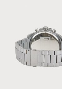 Relógio de pulso em aço inoxidável prateado com bracelete articulado, texturas polidas e escovadas, apresentando uma caixa redonda e múltiplos botões.