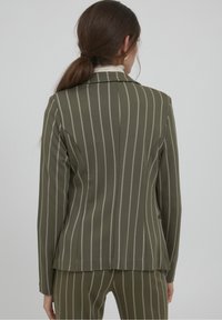 Blazer vert olive à rayures blanches verticales, design structuré, fermeture à un bouton et col à revers cranté ; coupe ajustée, adapté pour une tenue formelle.