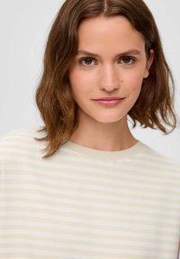Kremowa i beżowa bluzka w paski z okrągłym dekoltem. Gładka faktura, krótkie rękawy i subtelny wzór.