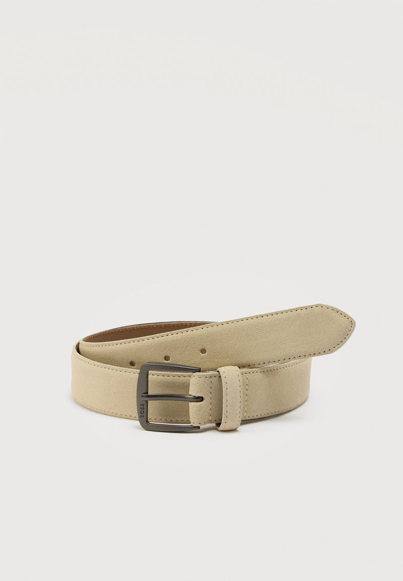 Ζώνη από μπεζ σουέτ με ορθογώνια πόρπη από σκουρόχρωμο μέταλλο, πολλαπλές τρύπες ρύθμισης και ραμμένο λουράκι, σε λευκό φόντο.