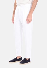 Pantaloni bianchi in lino con vita elastica, gambe affusolate e tasche laterali, abbinati a scarpe slip-on blu con suola in juta.