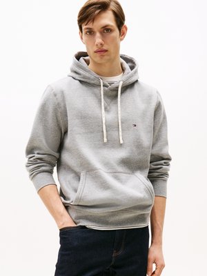 Sweatshirt cinza com capuz e cordões, bolso frontal, punhos canelados e detalhe discreto do logo. Combinado com jeans escuros.