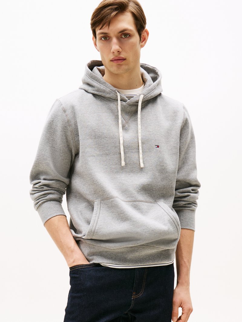Sweatshirt cinza com capuz e cordões, bolso frontal, punhos canelados e detalhe discreto do logo. Combinado com jeans escuros.