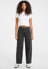 Vaqueros negros de corte holgado con una cintura alta, combinados con una camiseta corta blanca que presenta un pequeño diseño de estrella negra. Zapatillas blancas completan el conjunto.