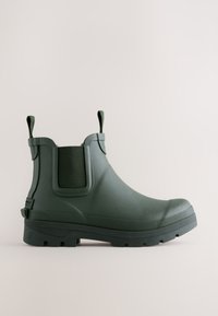 Botte de pluie mate vert foncé à la cheville avec languettes pour enfiler, semelle épaisse à crampons et panneaux latéraux élastiques sur fond clair uni.