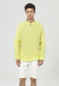 Linnen overhemd in felgeel met een bandkraag, lange mouwen en knoopsluiting. Gepaard met witte shorts, eenvoudig ontwerp, lichtgewicht textuur.
