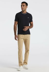 Marineblauwe kobaltkleurige short-sleeve overhemd met witte kraagdetails, gecombineerd met beige chino's en witte sneakers, met een subtiel logo op de borst.