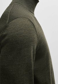 Oliwkowy sweter z dzianiny z golfem pokazany z okolicy ramienia, z widocznym ściegiem i teksturowanym materiałem.