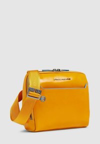 Sac à bandoulière synthétique jaune avec une texture lisse, des accents bleus, une fermeture éclair et une sangle réglable. Comprend une poche avant.