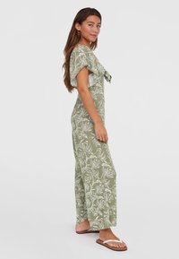 Combinaison vert olive avec un motif floral blanc, manches courtes évasées et un lien à l'avant. Tissu léger, coupe décontractée et jambes larges.