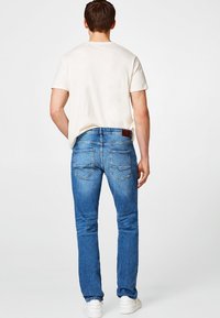 Ljusblå smala jeans med en svagt blekt textur, två bakfickor och en brun läderlapp vid midjan, bärs med en ljusbeige t-shirt.