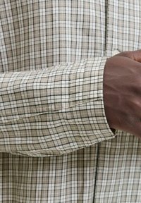 Langärmliges Hemd im beige-weißen Karomuster. Hergestellt aus weichem Stoff, mit Knopfverschluss und Detail an den Manschetten.