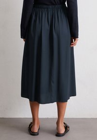Dunkelgrüner Midirock mit elastischem Bund, weichem Stoffgefühl und fließender Silhouette. Getragen mit flachen schwarzen Sandalen.