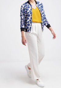 Vadderad bomberjacka med blå blommönster, svarta ribbade muddar; gul v-ringad topp; vita vida byxor; vita sneakers.