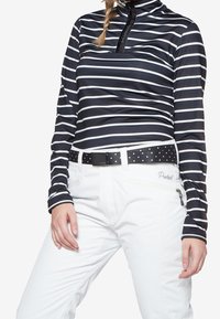 Persona che indossa una maglietta a righe orizzontali bianca e nera a maniche lunghe e pantaloni bianchi con una cintura nera decorata con pois bianchi.