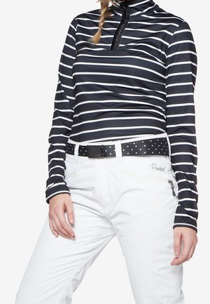 Personne portant un chemisier à rayures horizontales noir et blanc à manches longues et un pantalon blanc avec une ceinture noire à pois blancs.